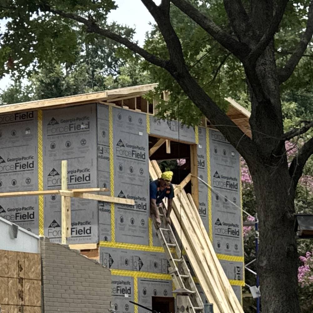 Crew member on a ladder sheathing a second-story addition