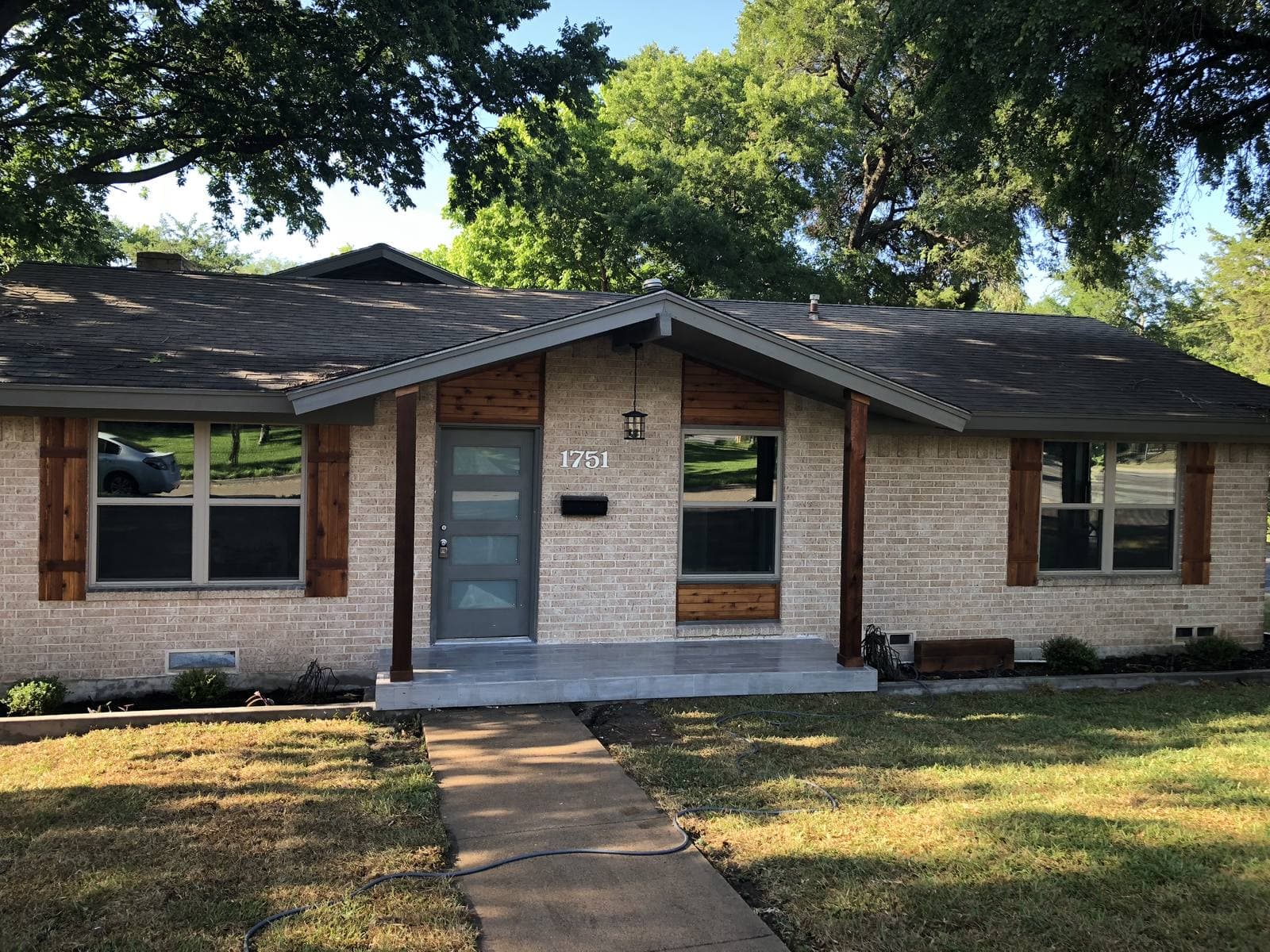 Light brick ranch home with cedar shutters and a gabled front porch