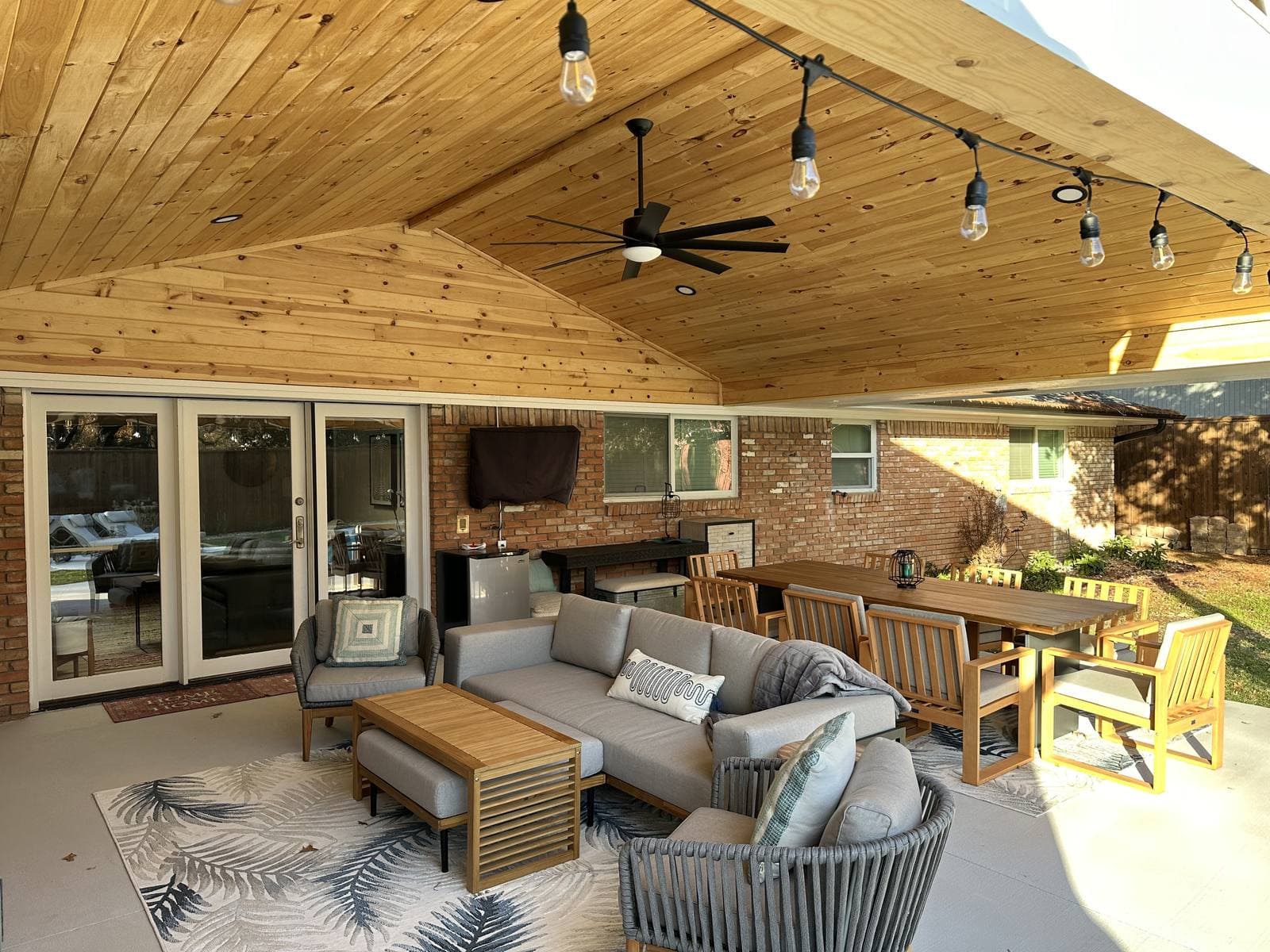 Covered patio with a vaulted cedar ceiling, string lights, and outdoor seating and dining