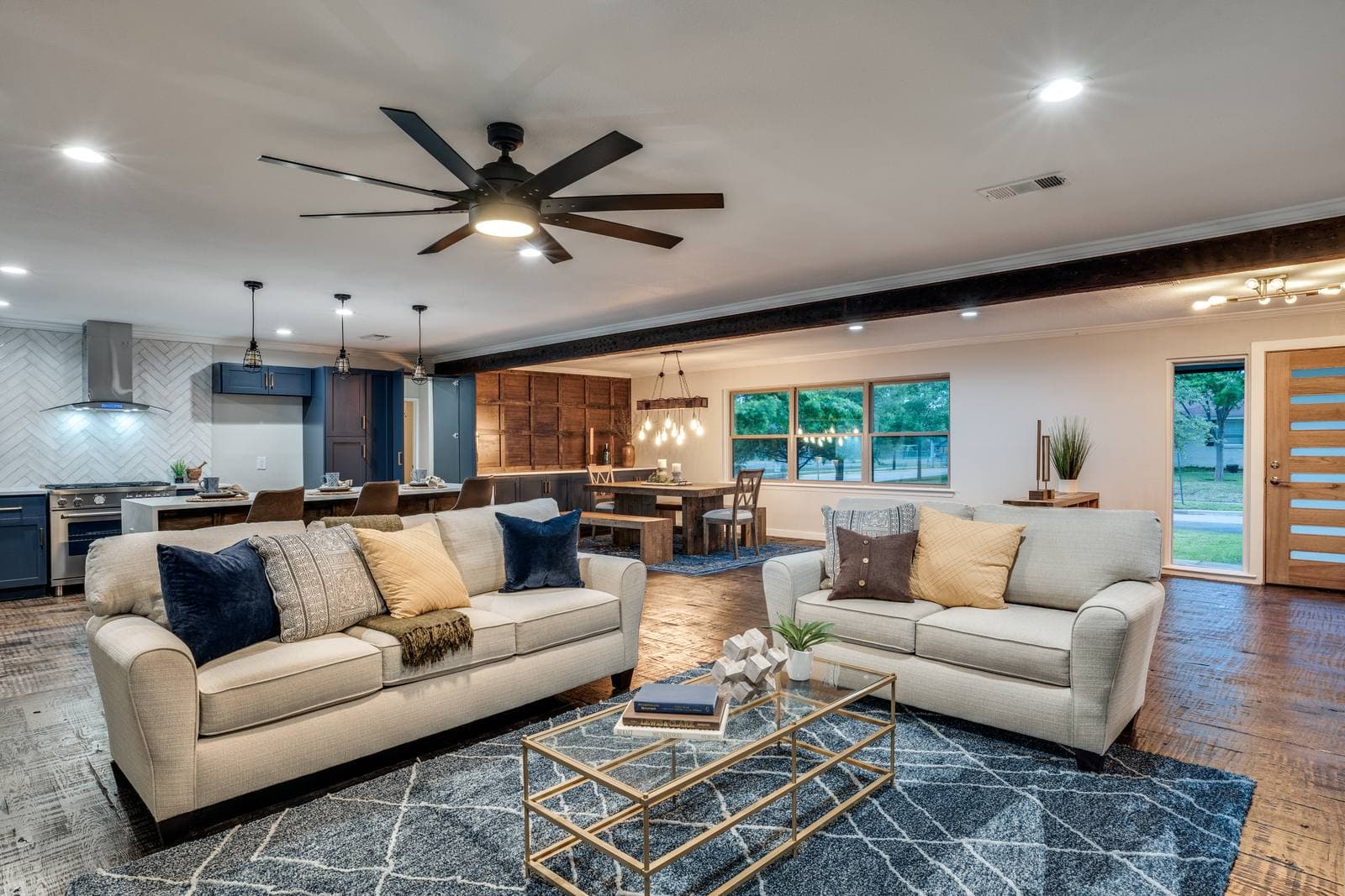 Open living and dining area with hardwood floors, a dark ceiling beam, and a kitchen beyond