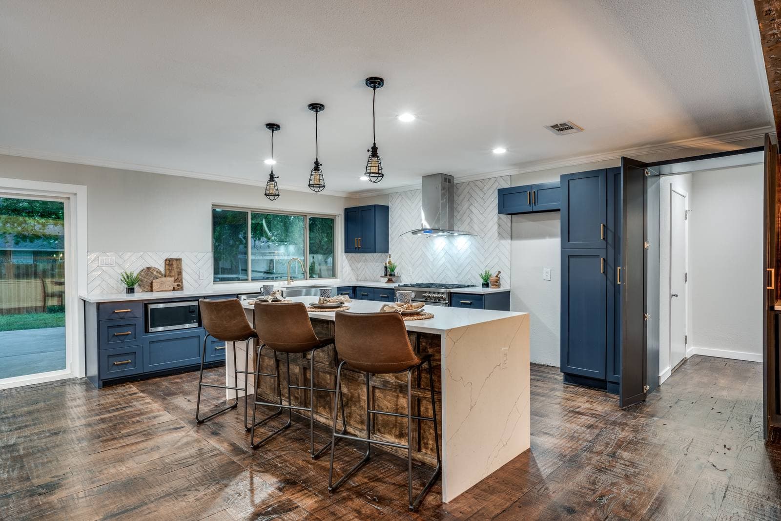 Kitchen with navy cabinets, a waterfall-edge island, and herringbone tile backsplash