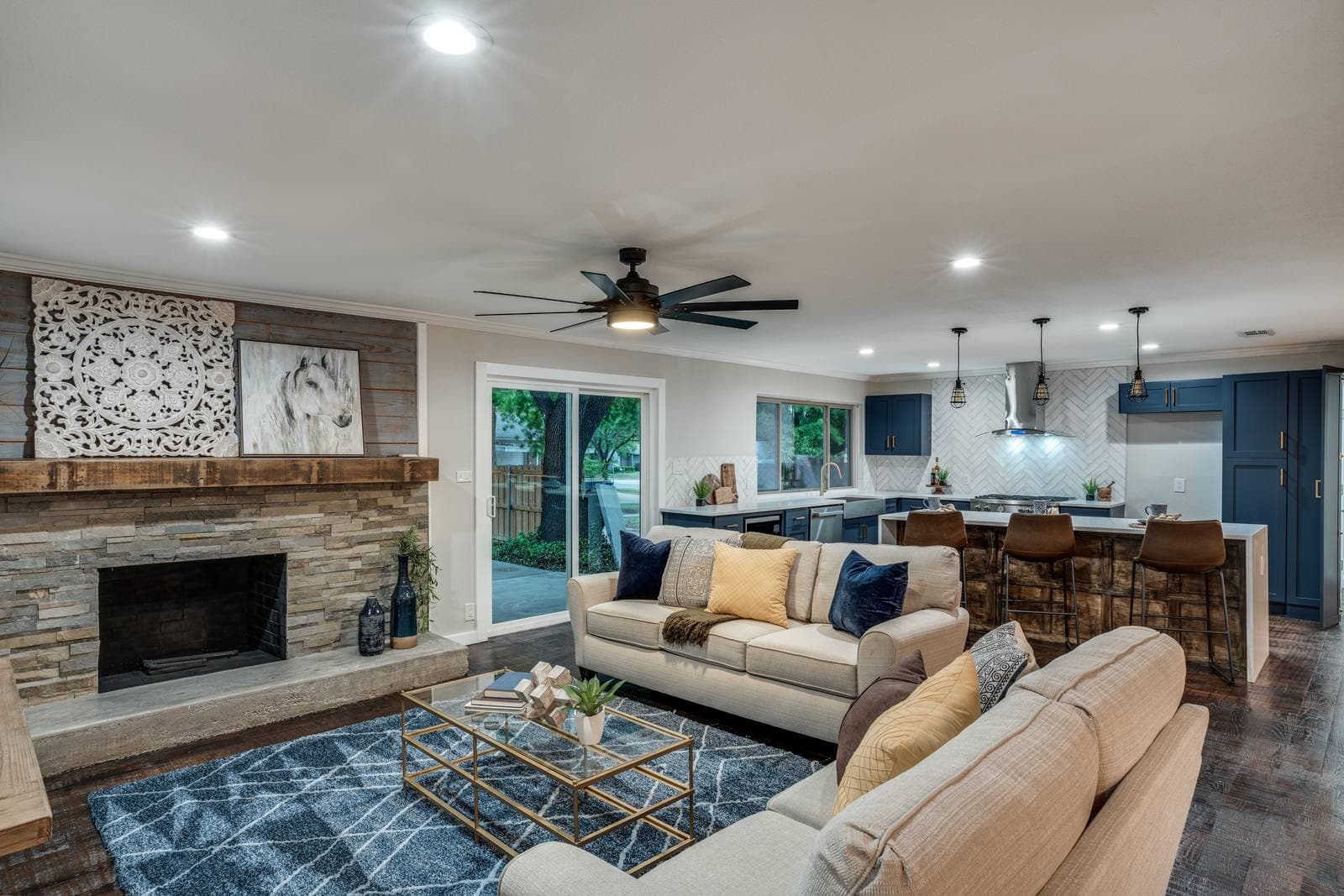 Living room with a stacked-stone fireplace and reclaimed wood mantel, open to the kitchen